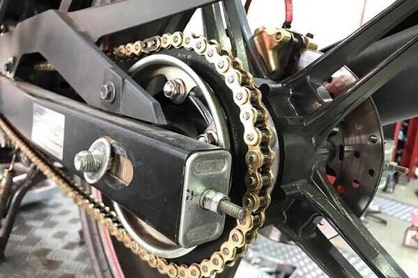 Hình ảnh một người thợ đang thao tác kiểm tra và điều chỉnh xích xe máy tại cửa hàng sửa chữa