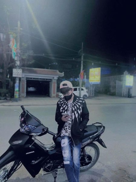 Chàng trai ngồi trên xe máy, che mặt một phần, tạo dáng lạnh lùng giữa không gian phố thị