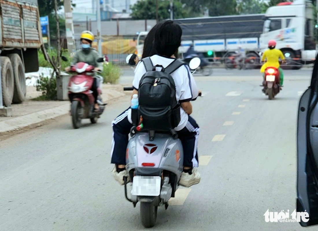 Hai học sinh không đội mũ bảo hiểm đi xe máy trên đường