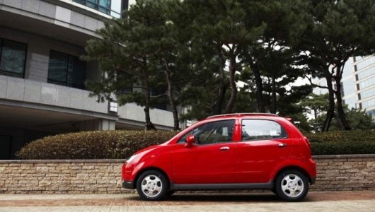 Hình ảnh một chiếc Daewoo Matiz màu đỏ nhỏ gọn đang đỗ trên vỉa hè thành phố