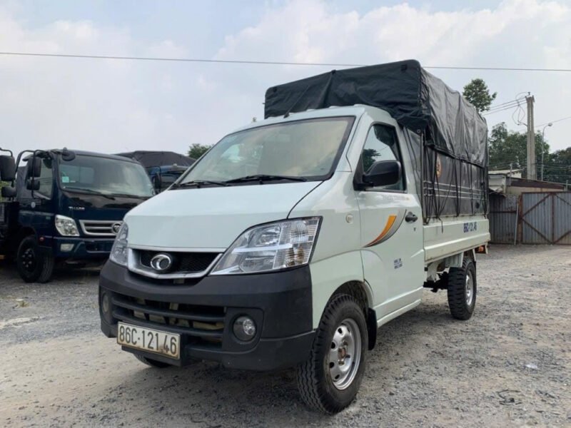 Hình ảnh một chiếc xe tải nhỏ cũ màu trắng với thùng kín đang đỗ trên đường nhựa