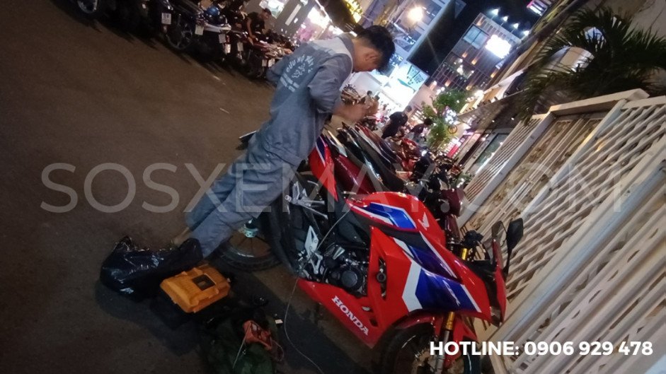 Hình ảnh một thợ sửa xe máy đang kiểm tra động cơ xe dưới ánh đèn ban đêm