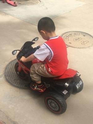 Một bé trai đang ngồi trên xe máy điện đồ chơi, thể hiện sự thích thú và năng động