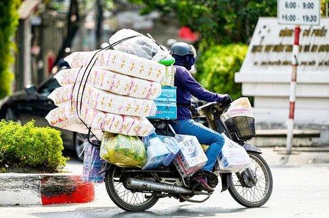 Một chiếc xe máy đang chở một kiện hàng lớn, thể hiện hành vi chở hàng quá khổ quá tải trên đường phố