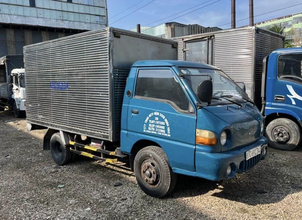 Một chiếc xe tải Hyundai H100 cũ màu trắng với thùng dài khoảng 3m13